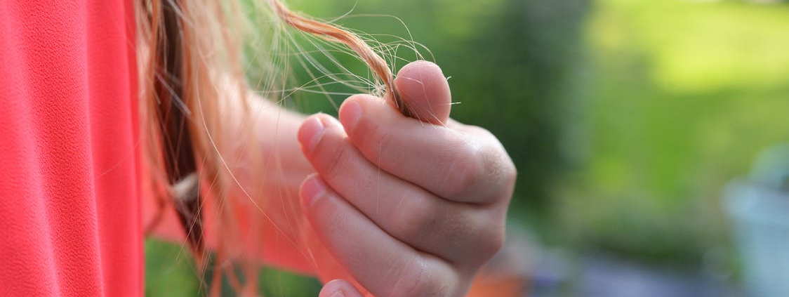 A woman in a red top holding a thin strand of hair after suffering from hair loss.